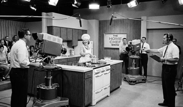 1960s TV studio kitchen set with camera crew filming a cooking show